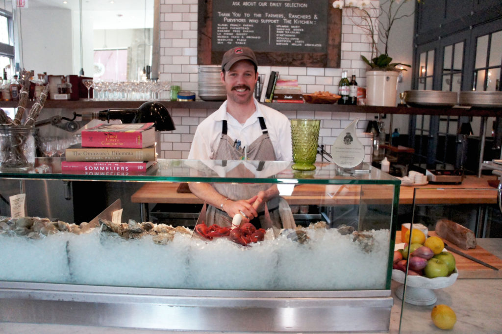 Chef Johnny Anderes stands behind the seafood bar at The Kitchen Chicago. Farmers, ranchers and other purveyors from whom the restaurant sources are listed on the chalkboard above his head. Photo: Bob Benenson/FamilyFarmed